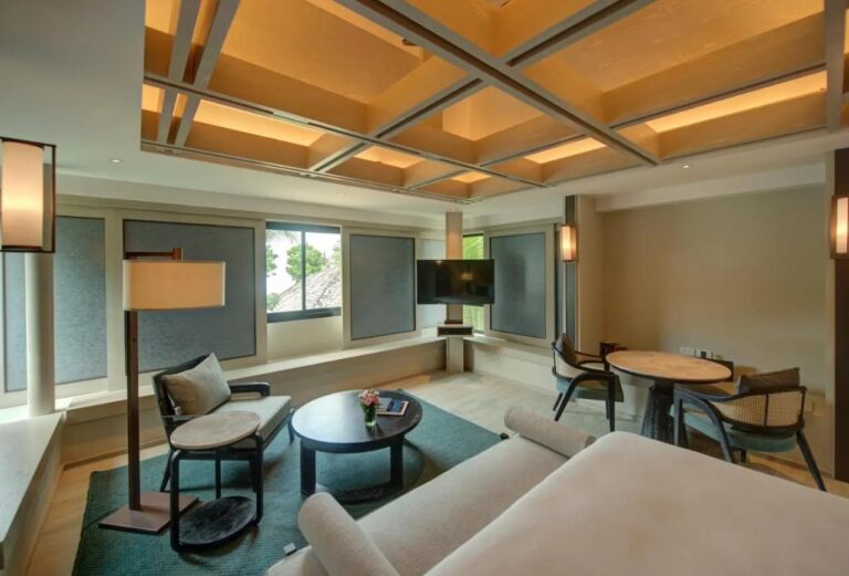 The sitting area of a room, with an armchair, a round coffee table and a table for two