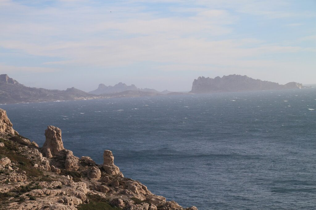 From the limestone rocks of Frioul in the foreground, a view across a rough, whitecapped sea to Maïre Island and the coast of Les Goudes, outlined in the haze.