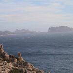From the limestone rocks of Frioul in the foreground, a view across a rough, whitecapped sea to Maïre Island and the coast of Les Goudes, outlined in the haze.