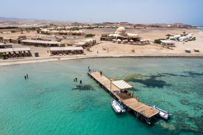 Aerial view of Marsa Shagra Village, with its jetty, two zodiacs and the village on the edge of the turquoise water