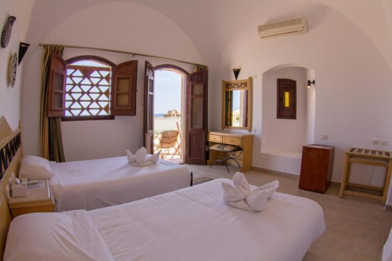 A twin room under a white vault, with the door open onto a terrace and the sea