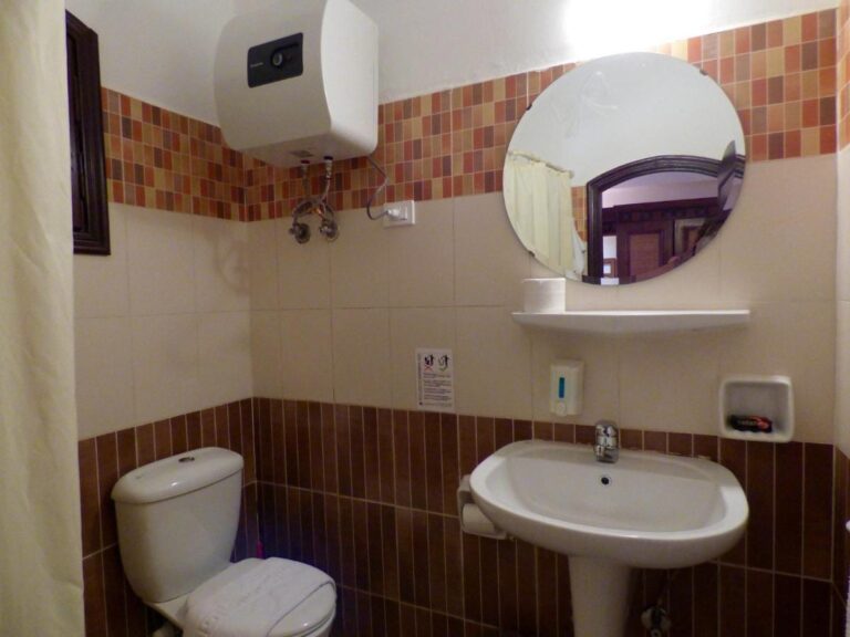 A bathroom with a sink, a toilet, a round mirror and a water heater
