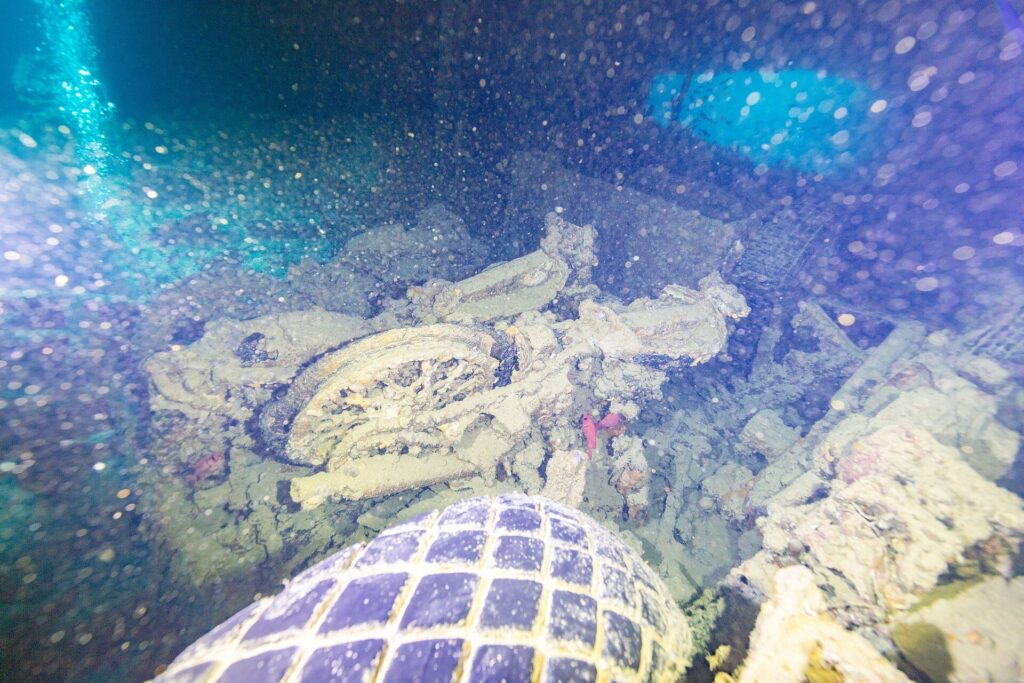 In a dark hold of the Thistlegorm, an overturned motorcycle behind a truck tire, lit by a dive light