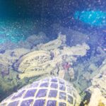 In a dark hold of the Thistlegorm, an overturned motorcycle behind a truck tire, lit by a dive light