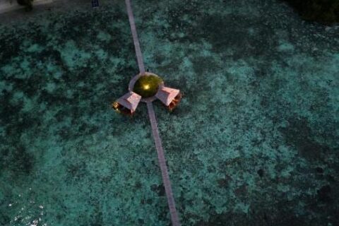 Aerial night view of a long wooden jetty running out from the beach, with two stilt huts halfway along
