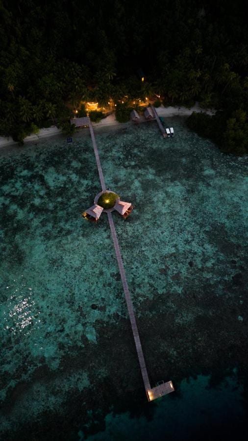 Aerial night view of a long wooden jetty running out from the beach, with two stilt huts halfway along