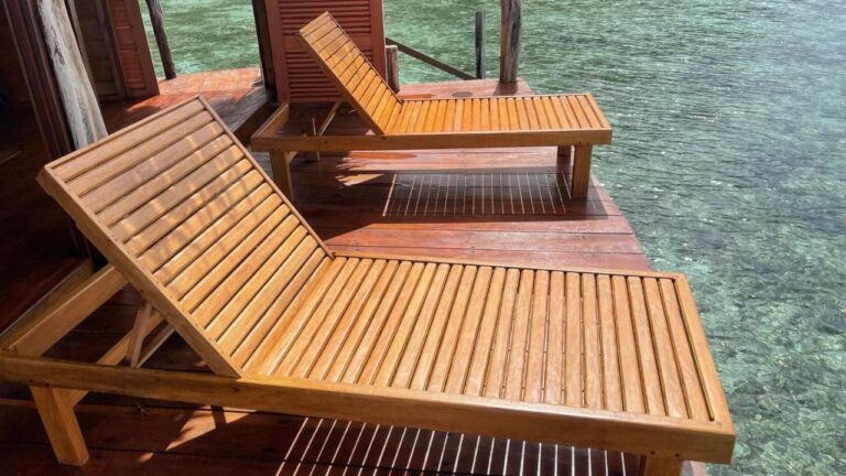 Two wooden sun loungers on a bungalow terrace, above clear water