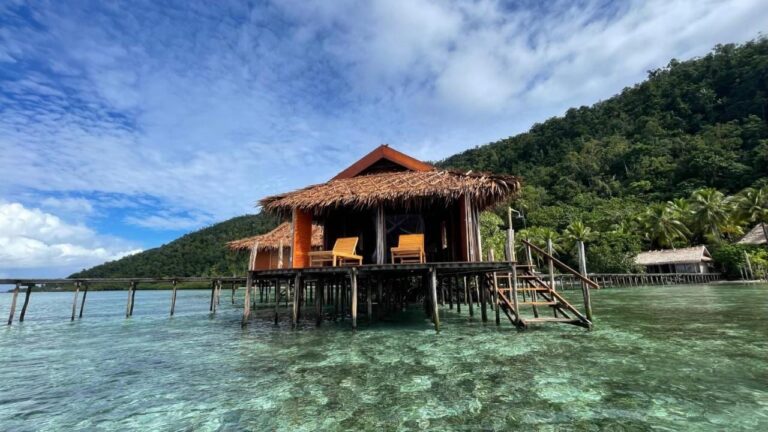 A Nyande Raja Ampat bungalow on stilts, above clear water, at the foot of a wooded hill
