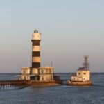 The Daedalus lighthouse, a black and white striped tower standing on the reef, with its buildings and metal jetty, at sunset