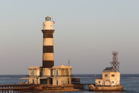 The Daedalus lighthouse, a black and white striped tower standing on the reef, with its buildings and metal jetty, at sunset