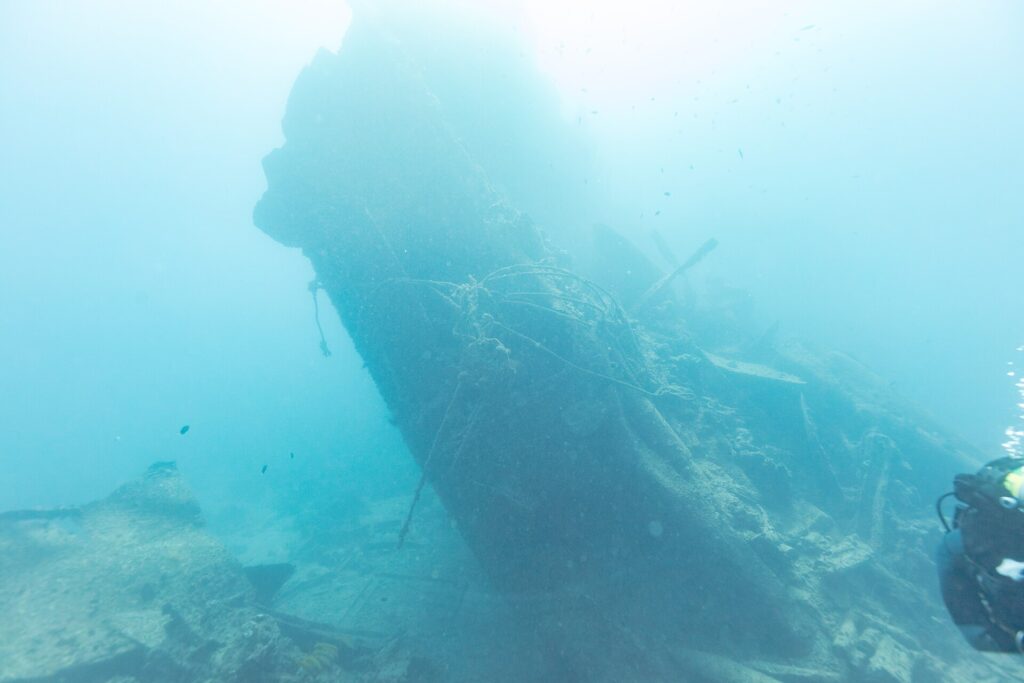 The broken stern of the Thistlegorm rising at an angle in the blue, a diver on the right