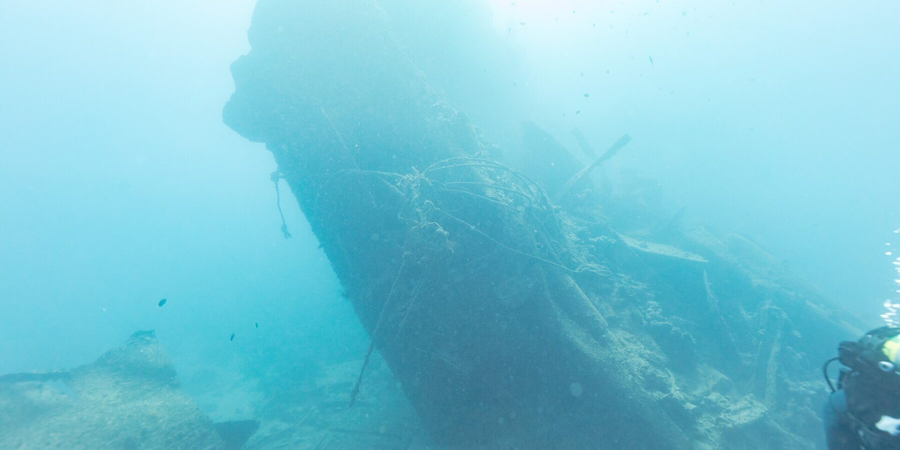 The broken stern of the Thistlegorm rising at an angle in the blue, a diver on the right