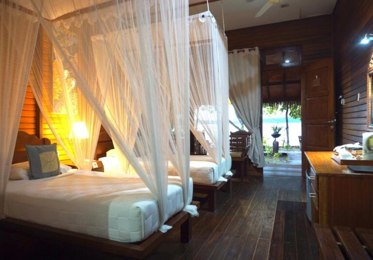 A twin room with beds under mosquito nets, wooden walls and a wooden floor