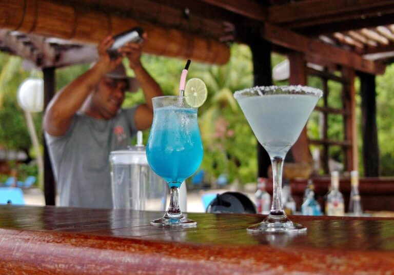 Two cocktails, one of them blue, on the wooden bar counter, in front of the bartender