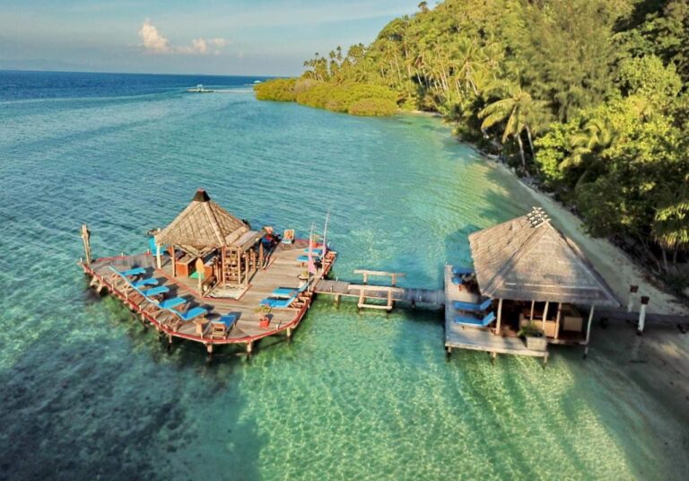 A deck on stilts with blue sun loungers, linked by a walkway to a pavilion on the beach