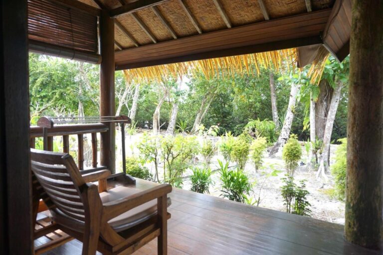 A wooden veranda with an armchair, facing a garden planted with trees