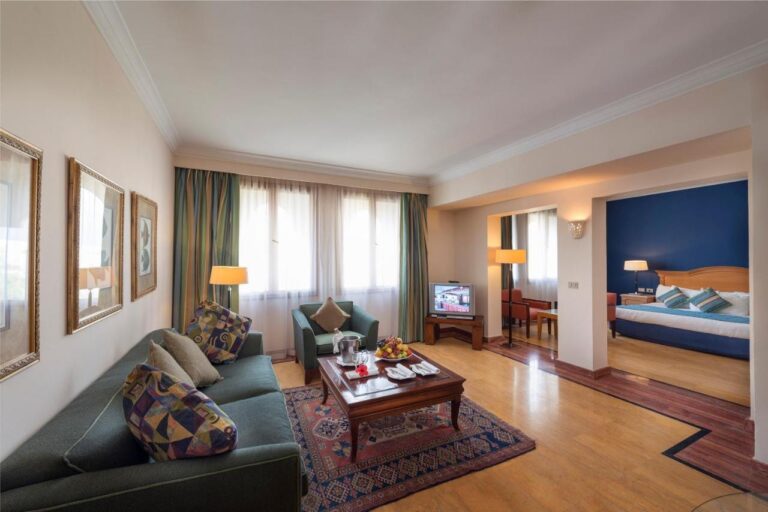 A living room with a green sofa and a rug, opening onto a bedroom with a blue wall