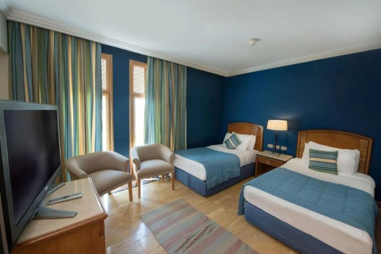A twin room with blue walls and two armchairs in front of the windows