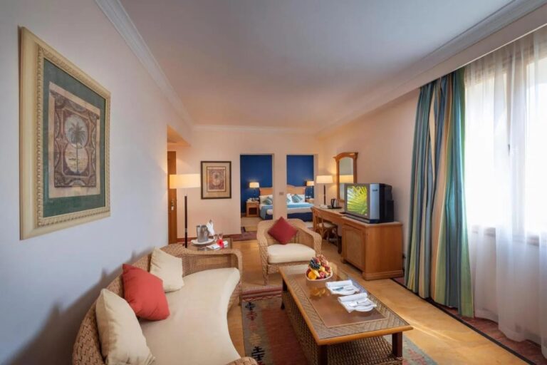 A living room with rattan furniture, with a blue-walled bedroom at the back