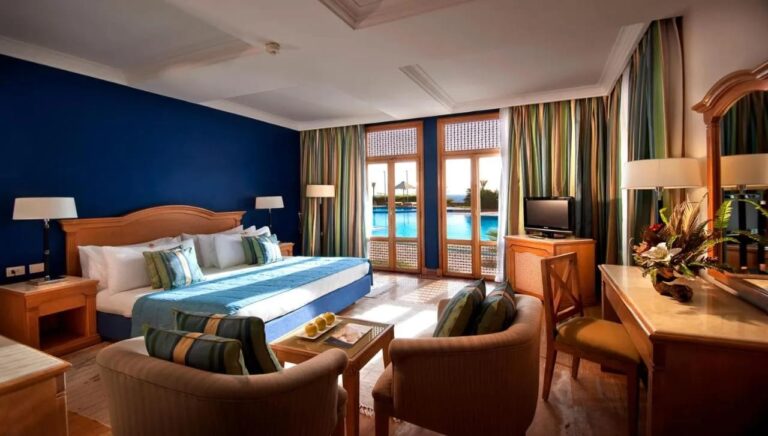 A room with a double bed, a blue wall and French windows onto the pool