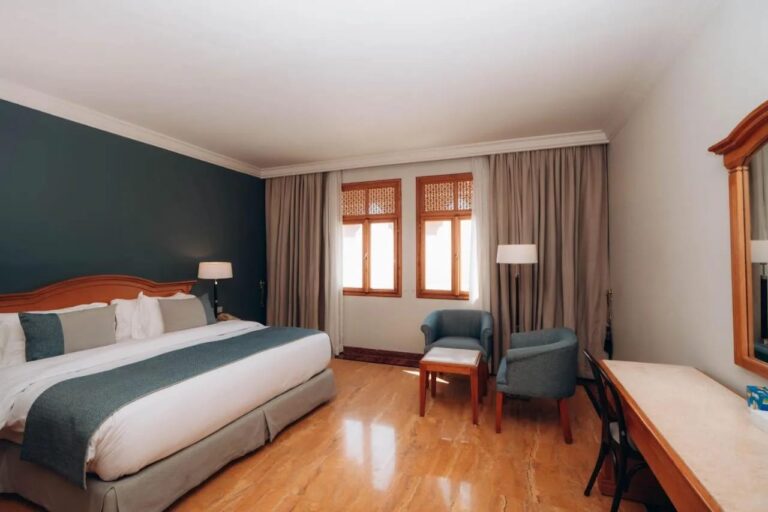 A room with a double bed, a dark green wall and two blue armchairs