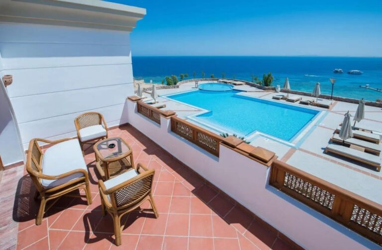 A terrace with rattan furniture above a large pool and the Red Sea, at Reef Oasis Beach Resort