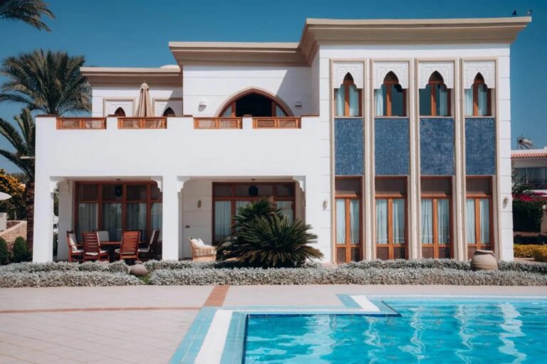 A white building at Reef Oasis Beach Resort, with arched windows and blue mosaic panels, in front of a pool