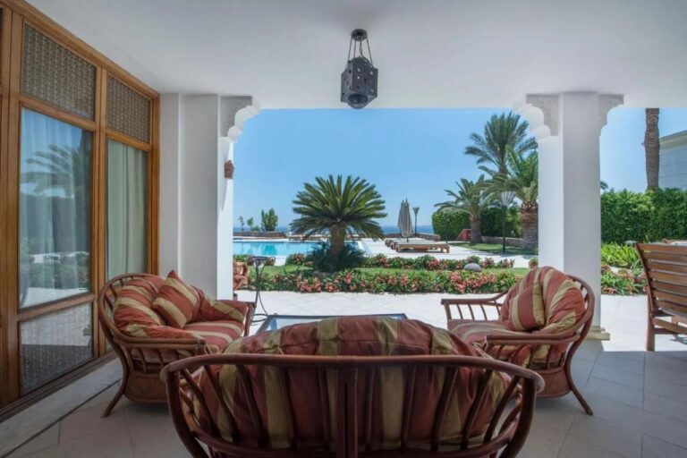 A covered terrace with rattan furniture, facing the flower garden, a pool and the sea