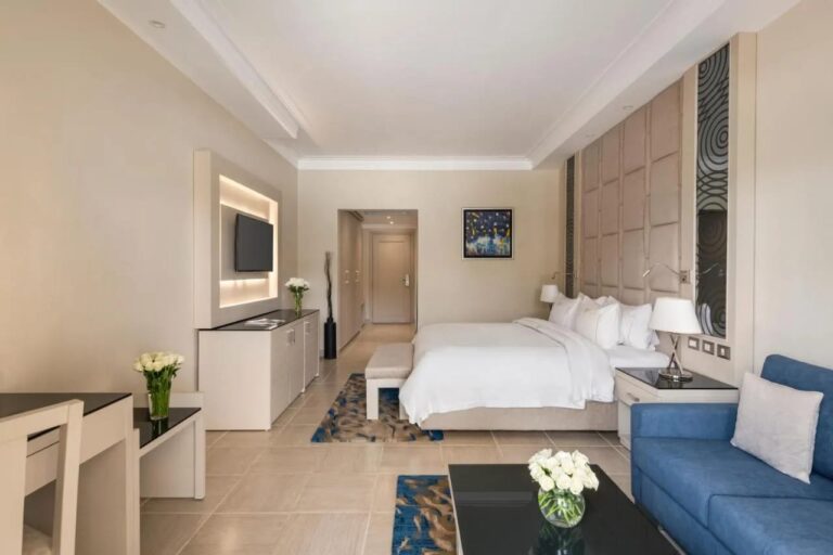 A room with a double bed, a blue sofa and a wall-mounted TV