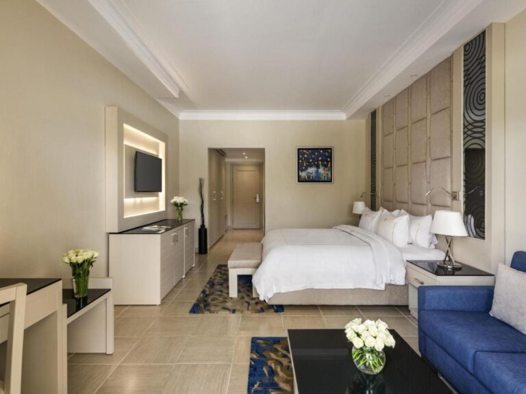 A room with a double bed, a blue sofa and white flowers on the table