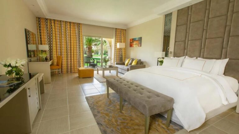 A room with a double bed opening onto the garden, with a bench at the foot of the bed
