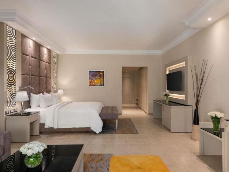 A room with a double bed, a wall-mounted TV and a desk area