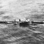 Black-and-white archive photo, taken from a plane, of a submarine running on the surface over a rippled sea, with a wake along the hull and the conning tower in the center.