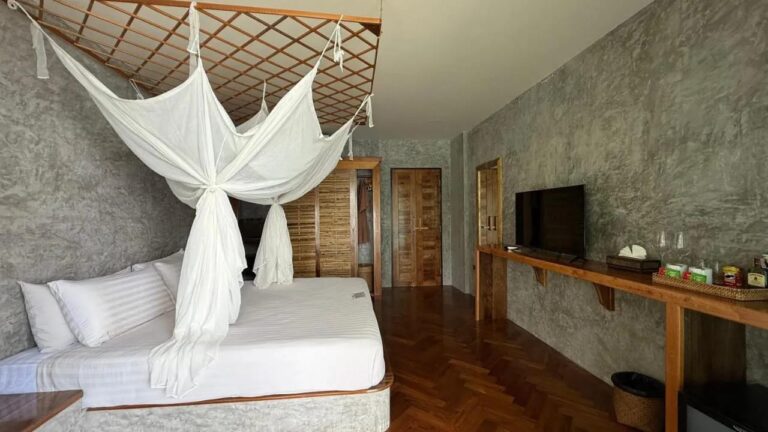 A room with a herringbone parquet floor, a bed under a mosquito net, a TV and a tea corner