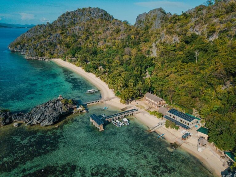 Aerial view of Sangat Island Dive Resort, with its beach, its jetty and its boats, at the foot of the cliffs