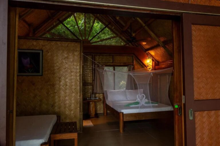 A room with woven bamboo walls, a double bed under a mosquito net and a single bed