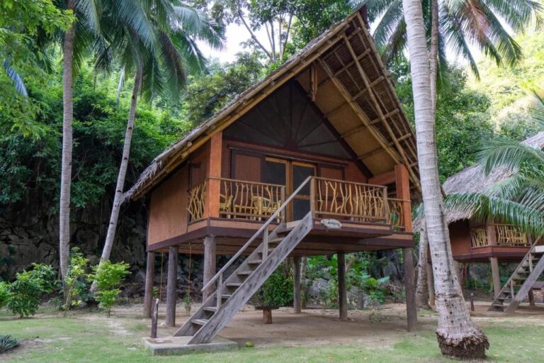 A bungalow on stilts at Sangat Island Dive Resort, with a wooden staircase, under the palm trees