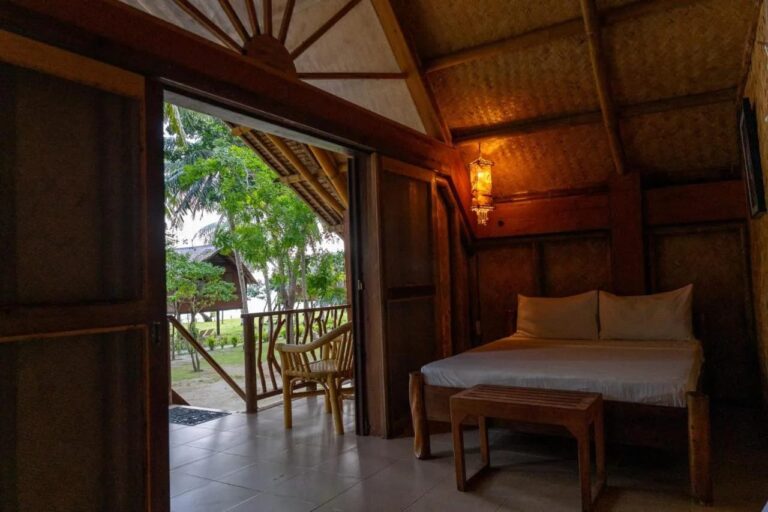 A room with a double bed opening onto the veranda, with a rattan armchair and the garden