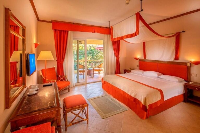 A room with a double bed under a white and orange canopy, opening onto a balcony