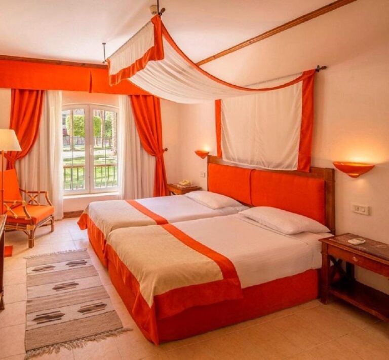 Two twin beds pushed together under a canopy, facing a window onto the garden