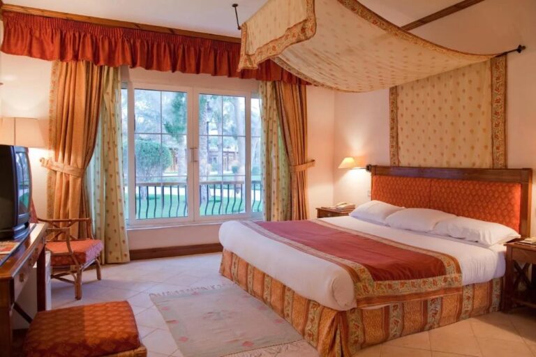 A room with a double bed under a floral canopy, with a picture window onto the garden