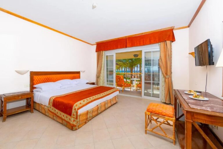 A room with a double bed opening onto a balcony, with the palm trees and the sea beyond