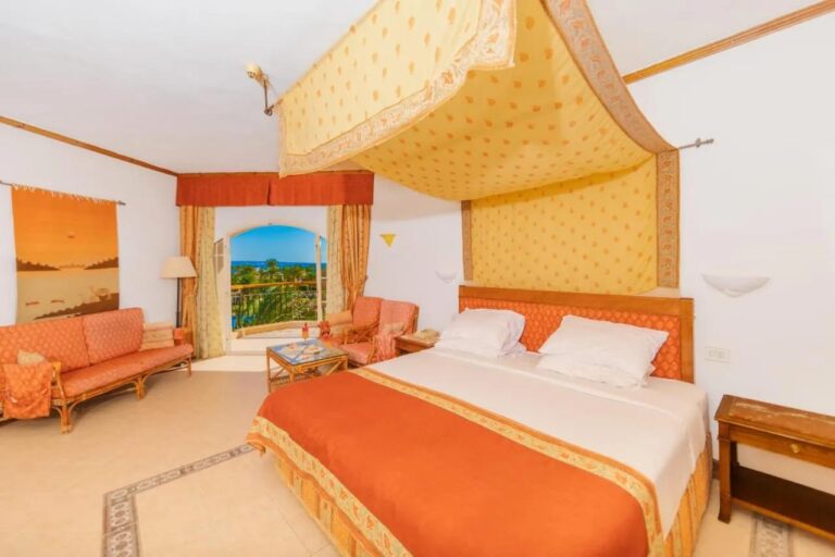 A room at Siva Grand Beach with a double bed under a yellow canopy, an orange lounge and the sea in the distance