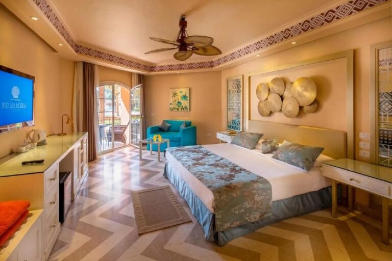A room with a double bed, a ceiling fan, a blue armchair and a herringbone floor