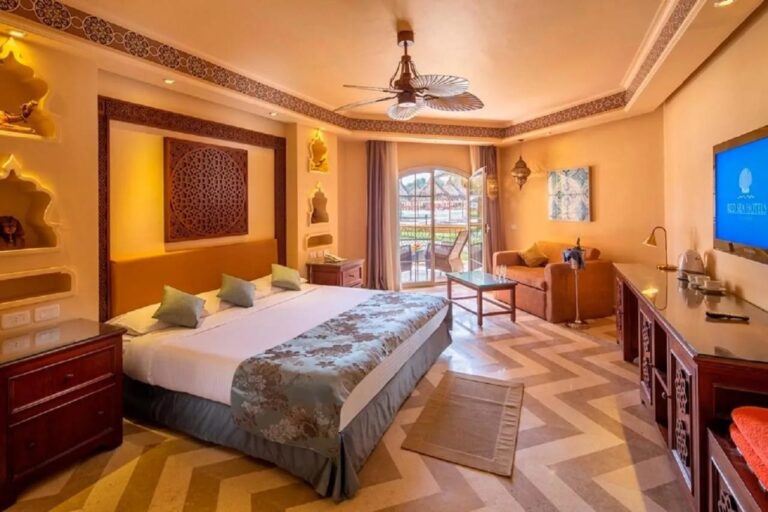 A room with a double bed, lit niches, a ceiling fan and a French window onto the balcony