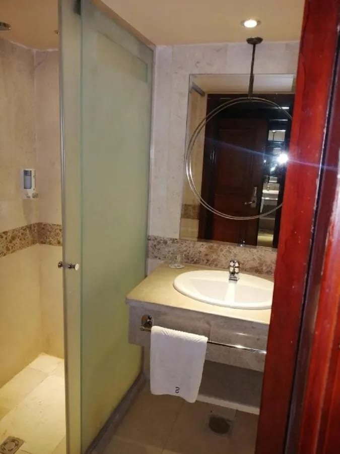A glass shower and a sink under a round mirror