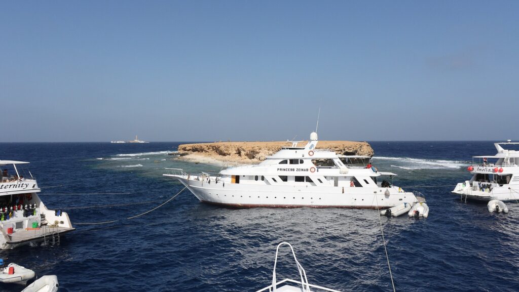 Three liveaboards moored in front of the flat islet of Small Brother, with the Big Brother lighthouse on the horizon