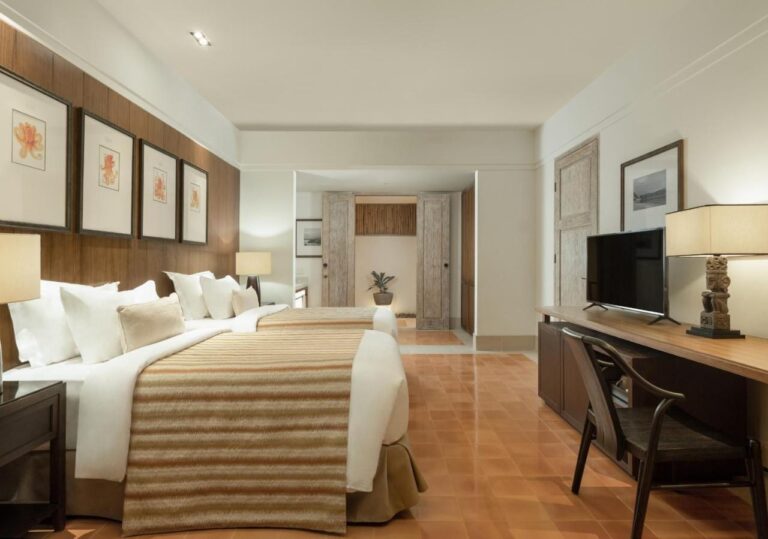A room with a double bed, a desk and prints on the wall