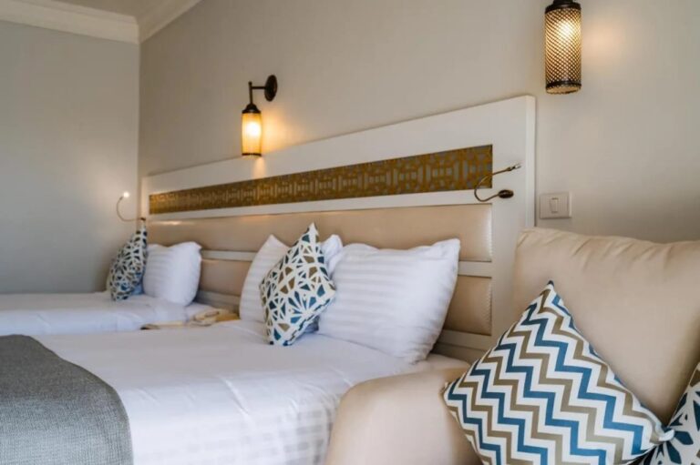 A long headboard with a golden frieze and lantern-shaped wall lights, above two beds