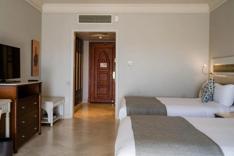 Two beds facing a wooden chest of drawers and the carved front door